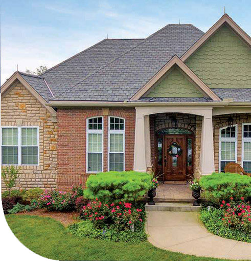 A house with a covered porch and a flower garden. The house has a brick and stone exterior.