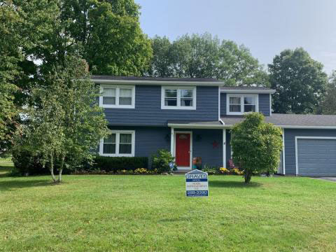 A blue house with white trim and a red door. A for sale sign in the front yard.
