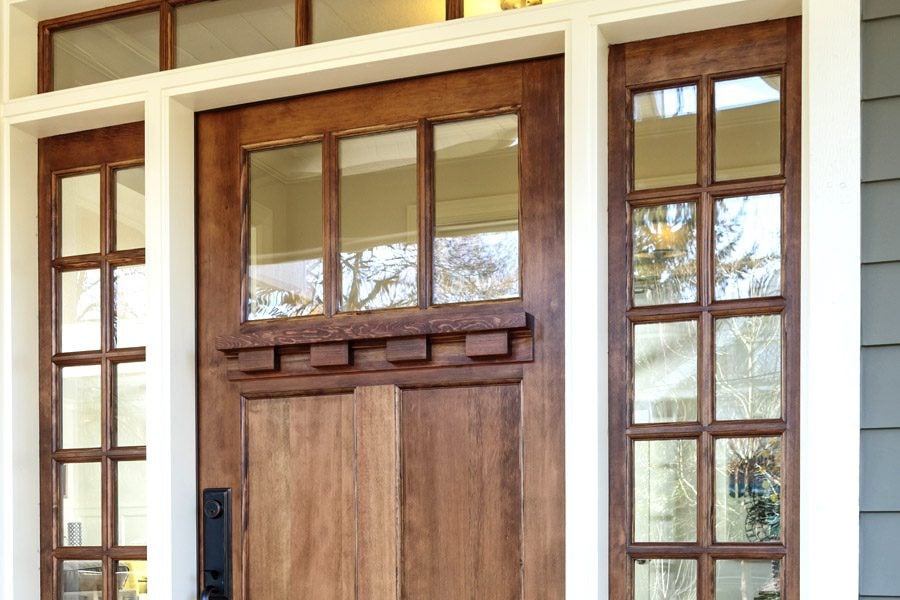 A brown wooden door with multiple windows on either side. The door has a decorative design.