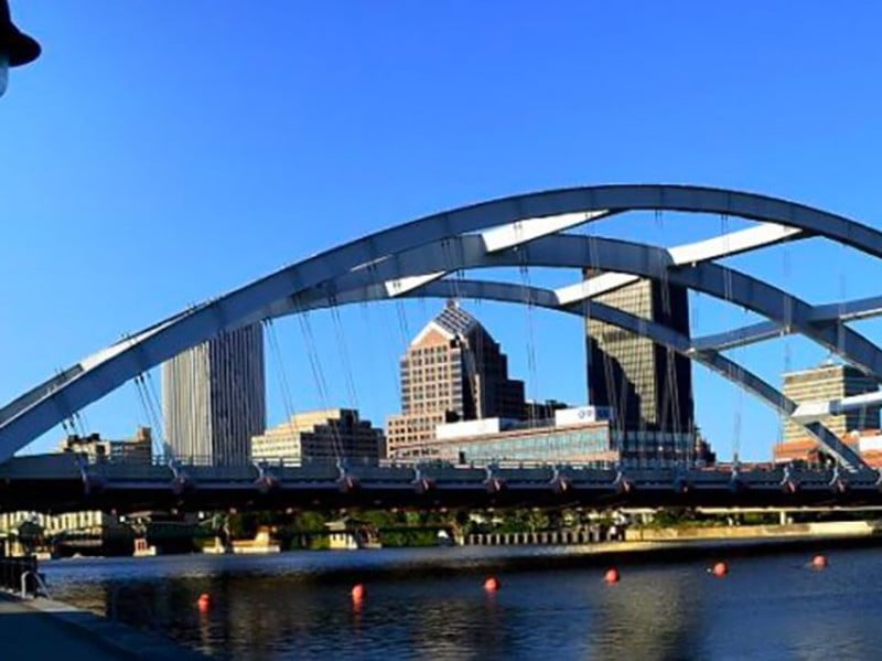 Cincinnati skyline with a large suspension bridge. The bridge spans a river with orange buoys.
