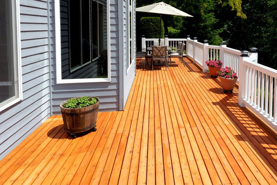 A wooden deck with patio furniture and potted plants. The deck is surrounded by a white railing.