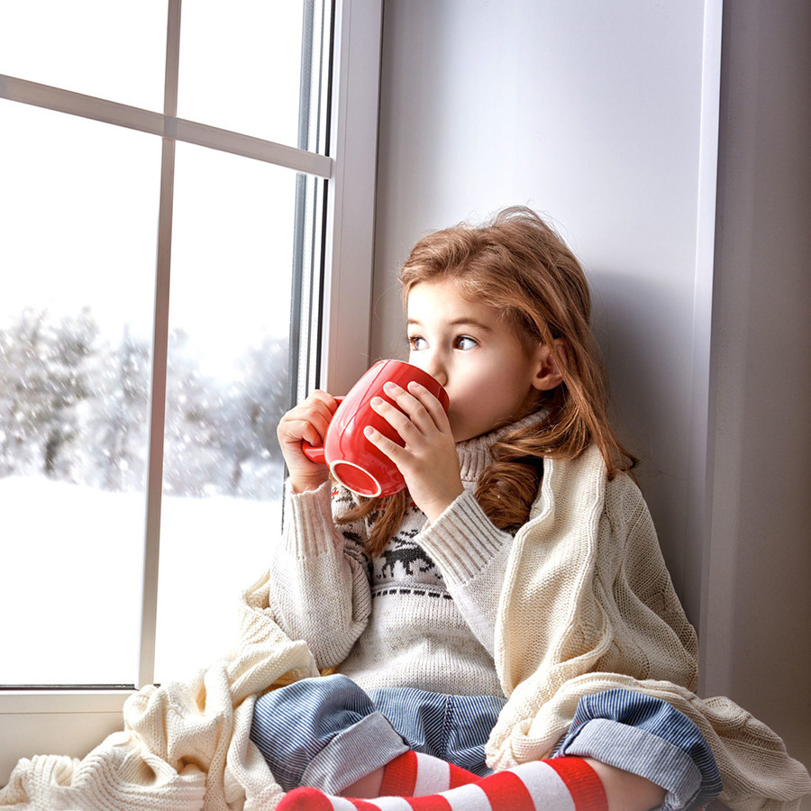 A young girl enjoys a warm drink by the window. She sits cozy and relaxed.
