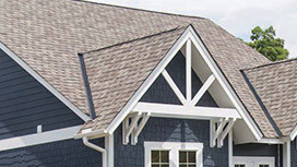 A roof with gray shingles and white trim on a modern house. The roof features a gable design.