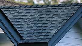 A close-up view of a roof's dark gray shingles and blue trim. The shingles are neatly arranged.