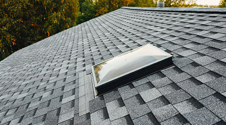 A roof with a skylight and gray shingles. The skylight is closed.