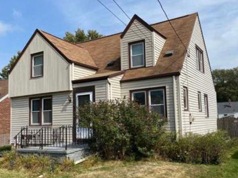 A two-story house with a brown roof and gray siding. The house has a small porch.