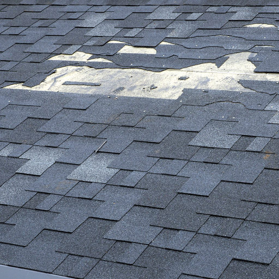 Damaged roof shingles. A section of the roof has missing pieces.