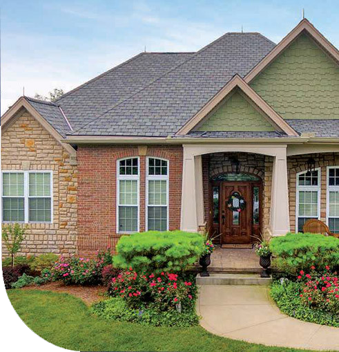 A house with a large front porch and bushes. The house has a gable roof and a stone exterior.