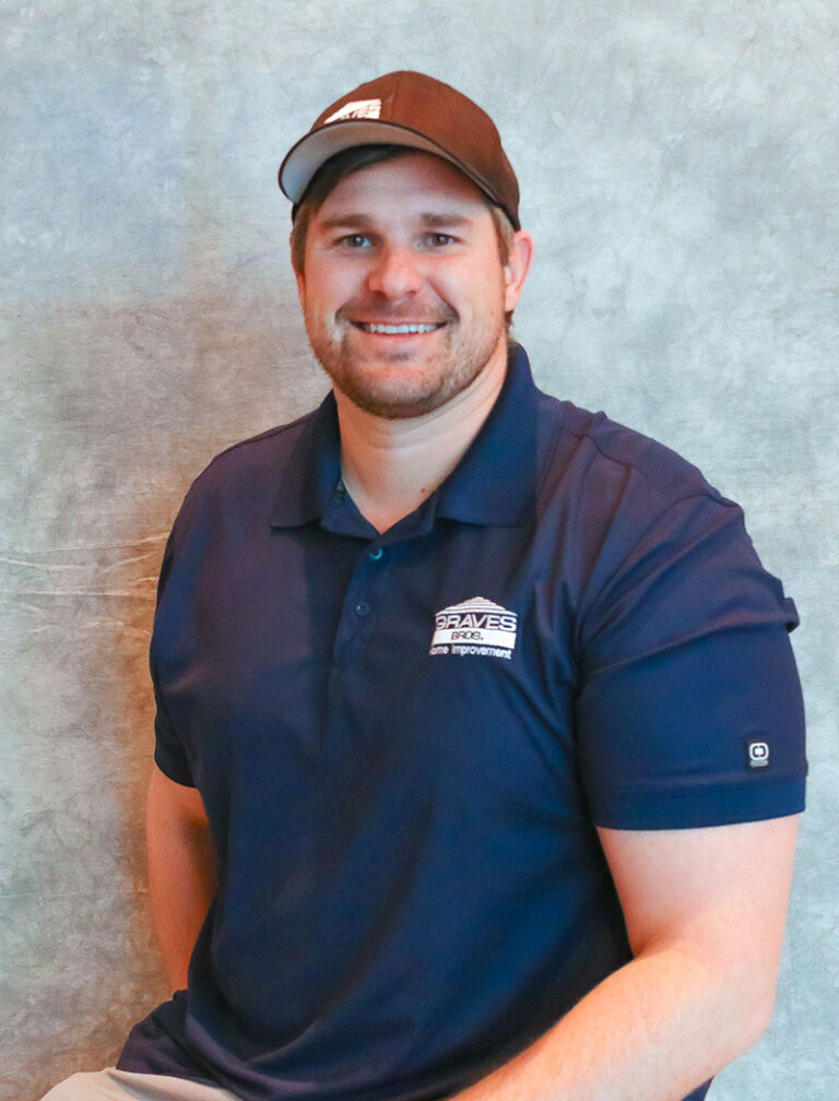 A man in a brown baseball cap and navy blue polo shirt with a white logo on the left side of his chest.