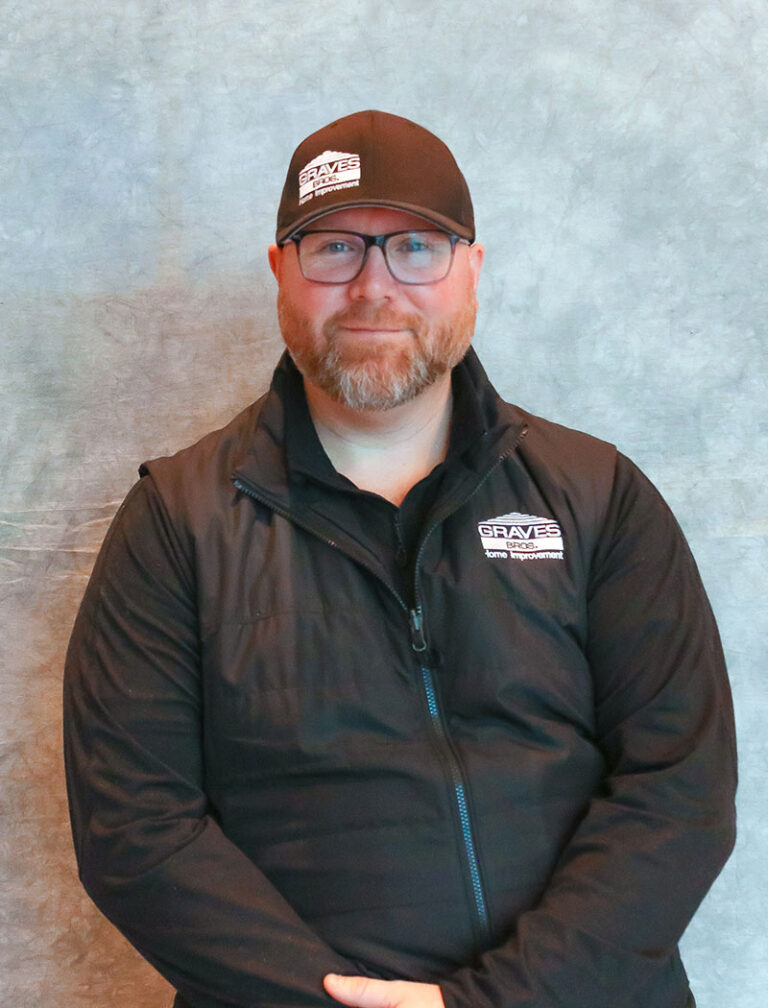 A man with glasses and a beard wearing a black jacket and baseball cap. He appears to be a staff member or representative of a company.