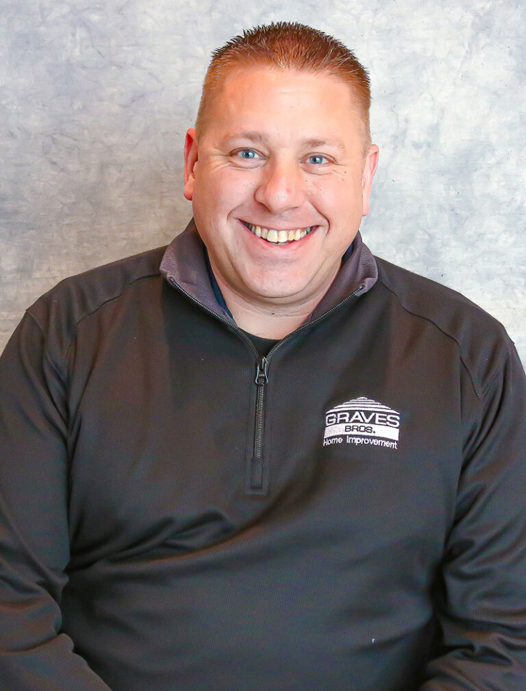 A man with short hair smiling at the camera. He is wearing a black quarter zip pullover with a logo on the chest.
