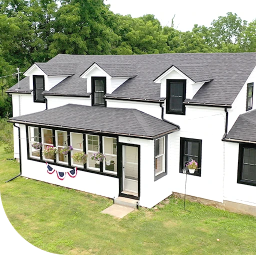 A black and white image of a house with a covered porch. The house has dormer windows and a sloping roof.