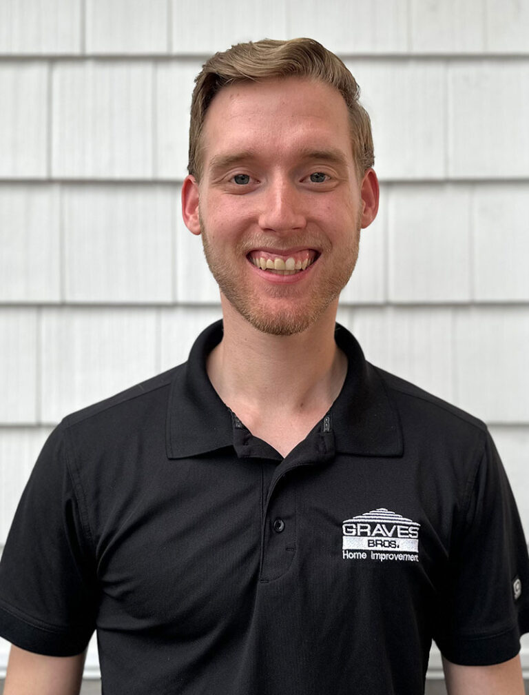 A man with short blonde hair wearing a black polo shirt with a company logo on the left chest