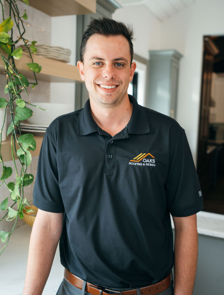 A man in a black polo shirt with a company logo. He is standing in an office setting.