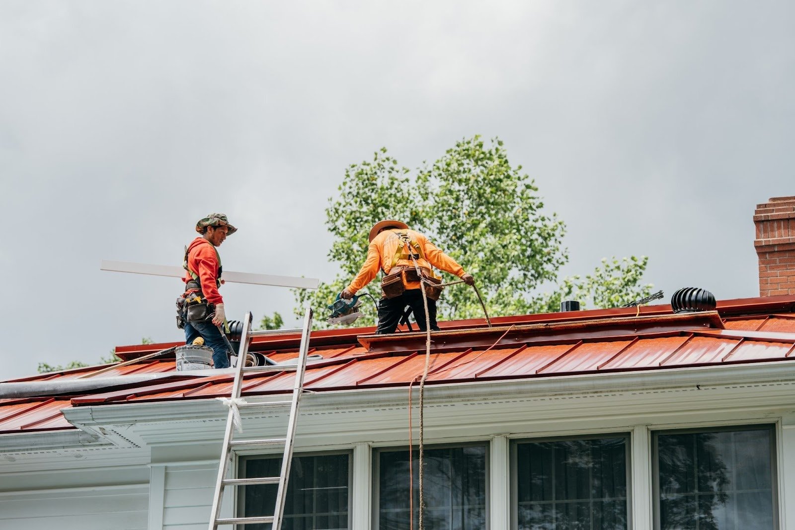 Two roofers in orange safety gear working on a roof. They are installing a metal roof.