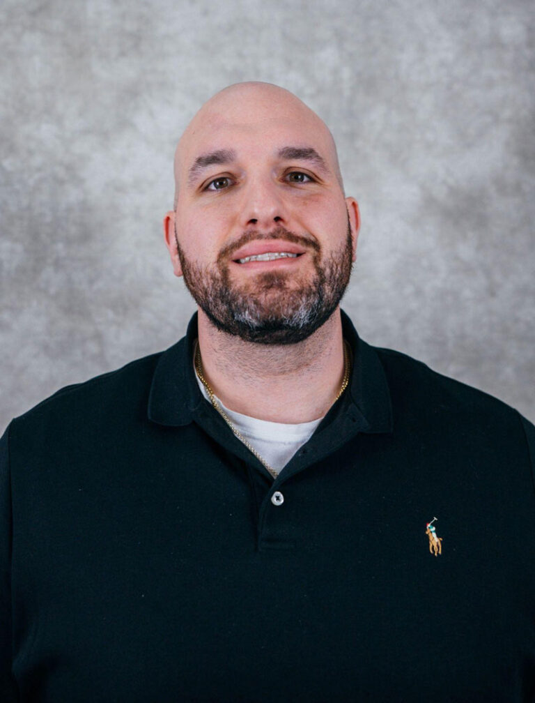 A bald man with a beard wearing a black polo shirt. He is smiling and looking at the camera.
