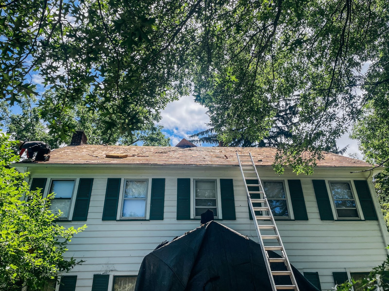 a white house with green shutters and a ladder on the roof