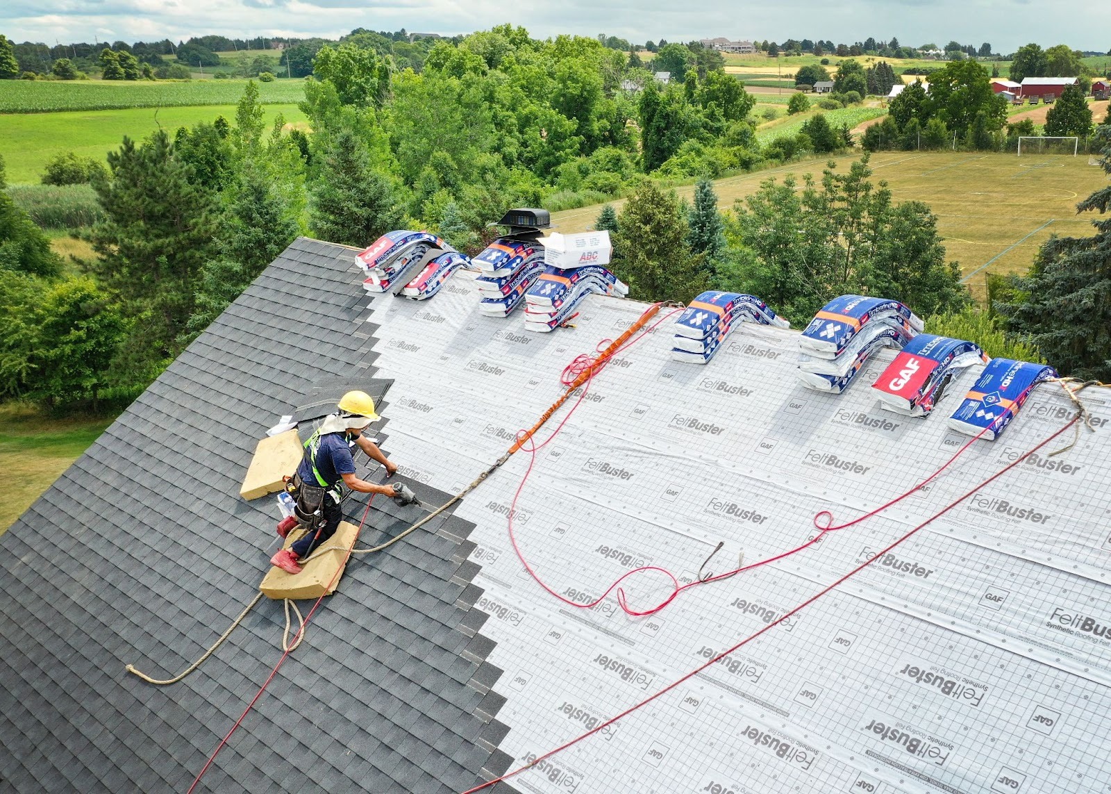 A roofer in a harness working on a roof. The worker is installing shingles.