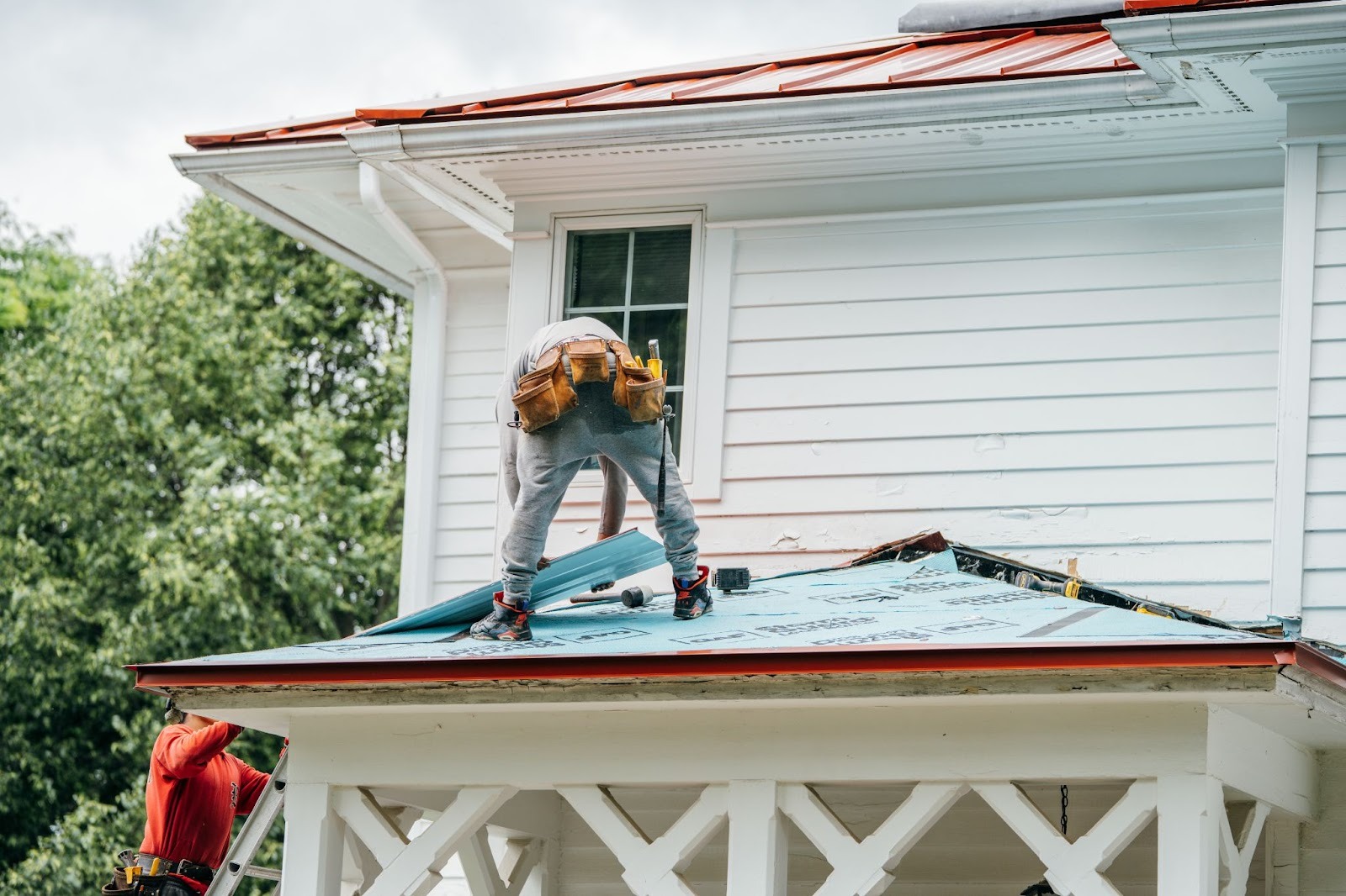 Two roofers working on a house. They are installing new roofing material.