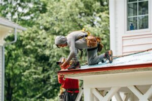 Two roofers working on a house roof. A roofer wearing gray kneeling on a roof.