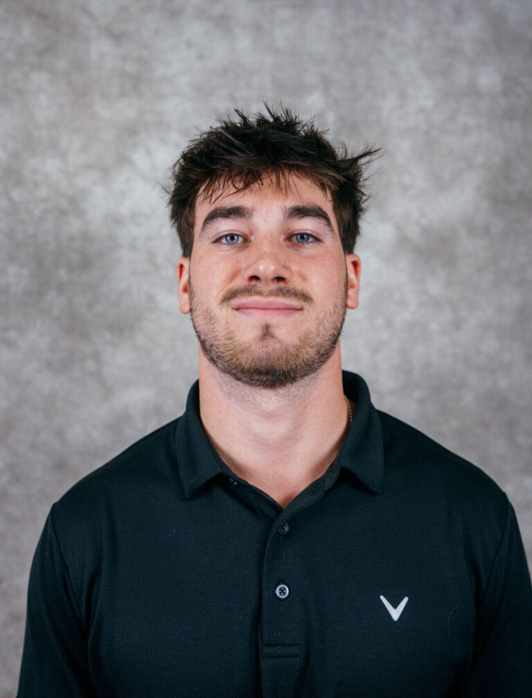 A young man with dark hair and a short beard wearing a black polo shirt with a white logo