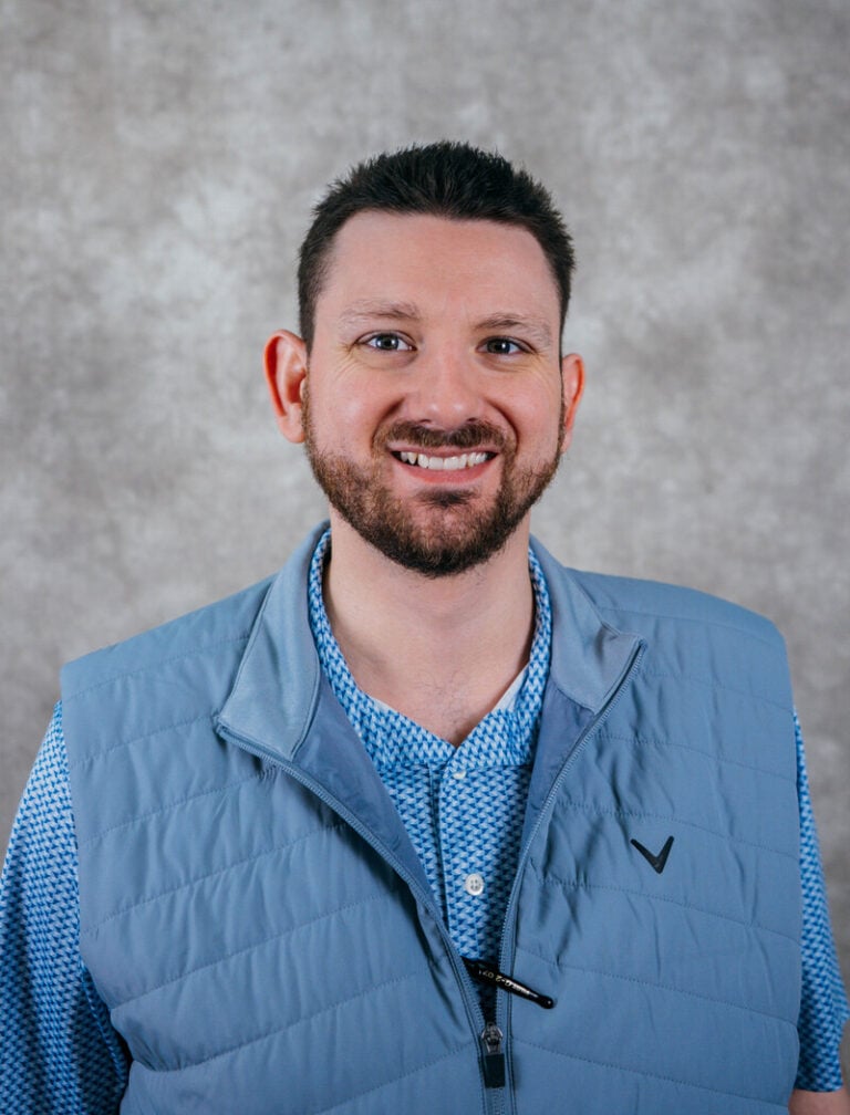 Man with short dark hair and beard wearing blue vest