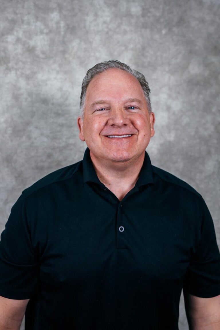 Portrait of a smiling man. He is wearing a black polo shirt.