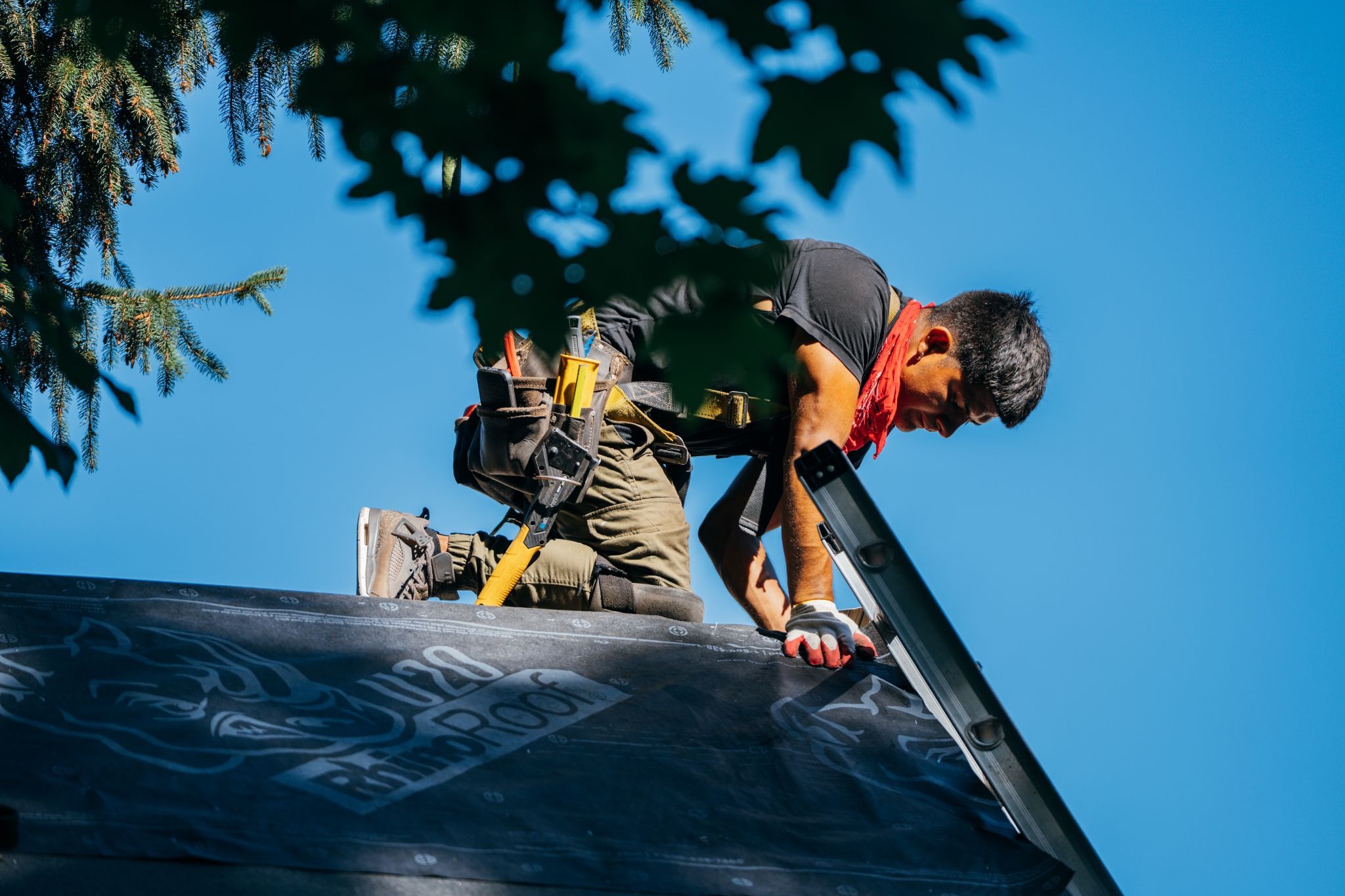 A man wearing a tool belt working on roof. He is focused on his work.