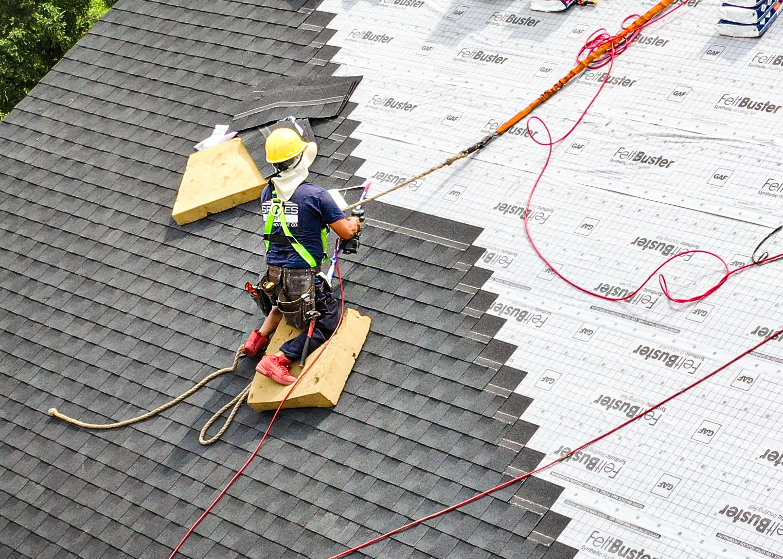A roofer in a harness and helmet on a roof. The worker is secured with ropes.