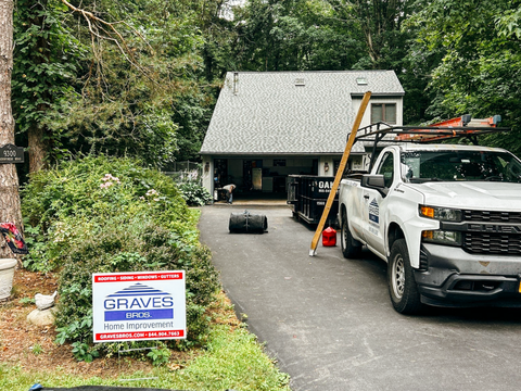 A white work truck parked in front of a house with a Graves Home Improvement sign in the yard.