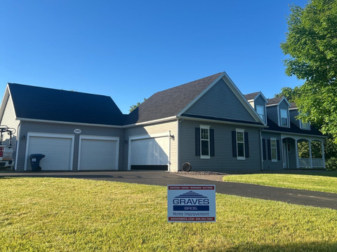 Gray house with three garage doors, roof installed, and a Graves Roofing sign in the front lawn.