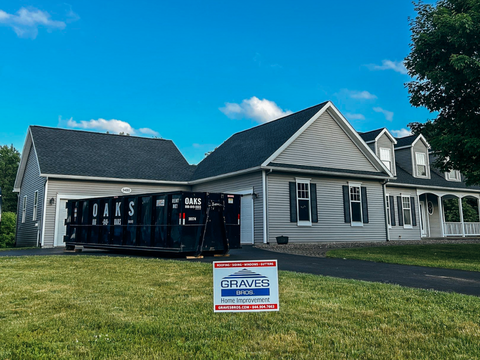 A newly installed dark shingle roof on a light-colored house with a landscaping sign in front.