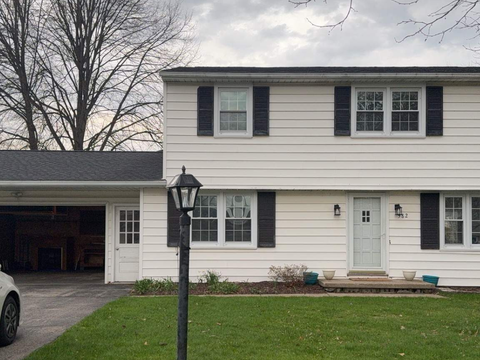 A picture of a white suburban two-story house with a front lawn, garage, and black shutters on the windows.
