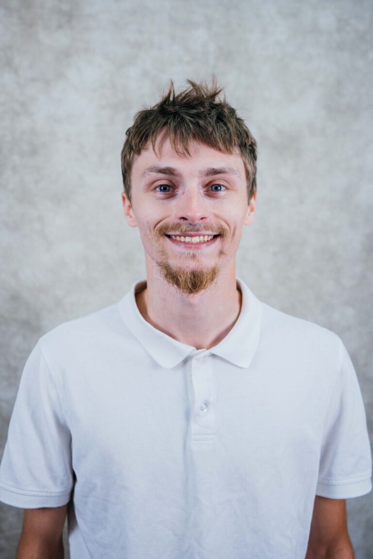 Portrait of a young man in a white polo shirt smiling at the camera.