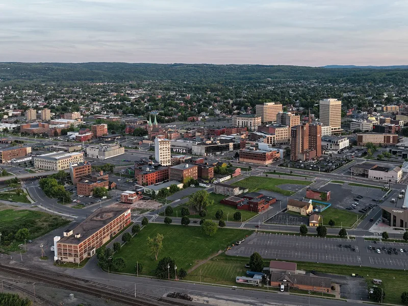 An elevated wide-angle view of a city with buildings, roads, and green spaces extending to the horizon.