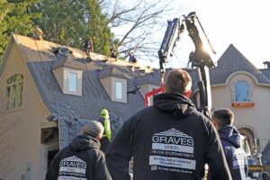 A team of roofing workers in black Graves hoodies is shown on the roof of a large house while a crane is visible. A close-up shows shingles and a worker near a chimney.