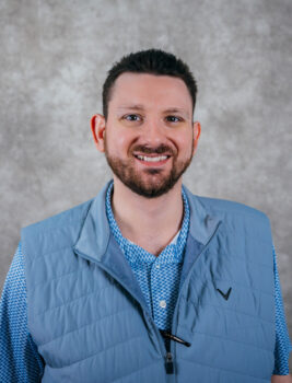 Man with short dark hair and beard wearing blue vest