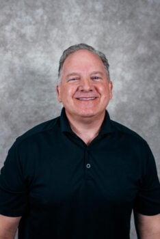 Portrait of a smiling man. He is wearing a black polo shirt.