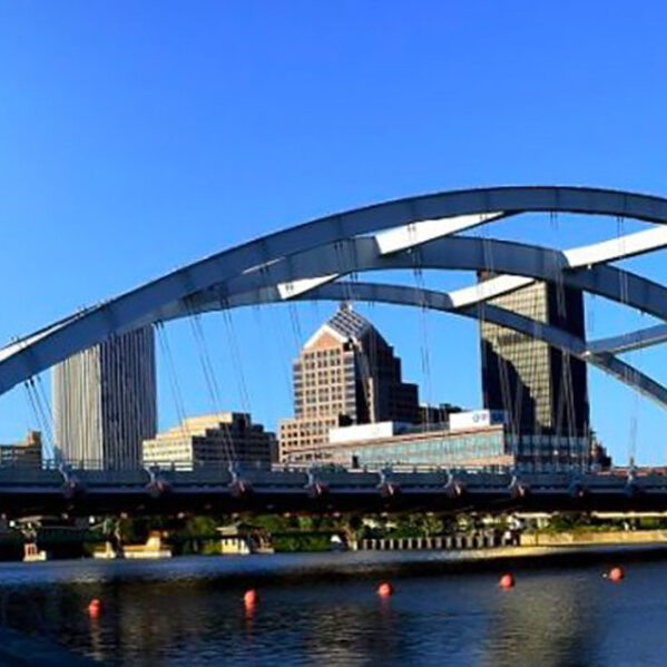 Cincinnati skyline with a large suspension bridge. The bridge spans a river with orange buoys.