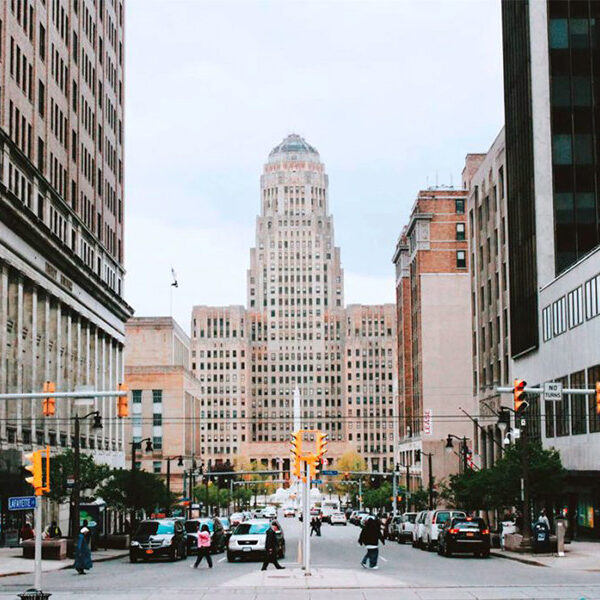 A city street with tall buildings and traffic lights. The street is lined with trees and cars.