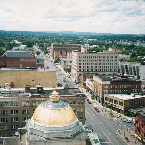 A city street with a large gold domed building. The building is surrounded by other buildings and trees.