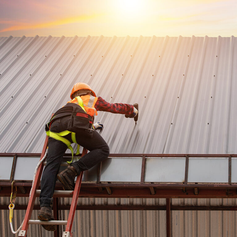 A construction worker wearing safety gear on a roof. The worker is using a tool.