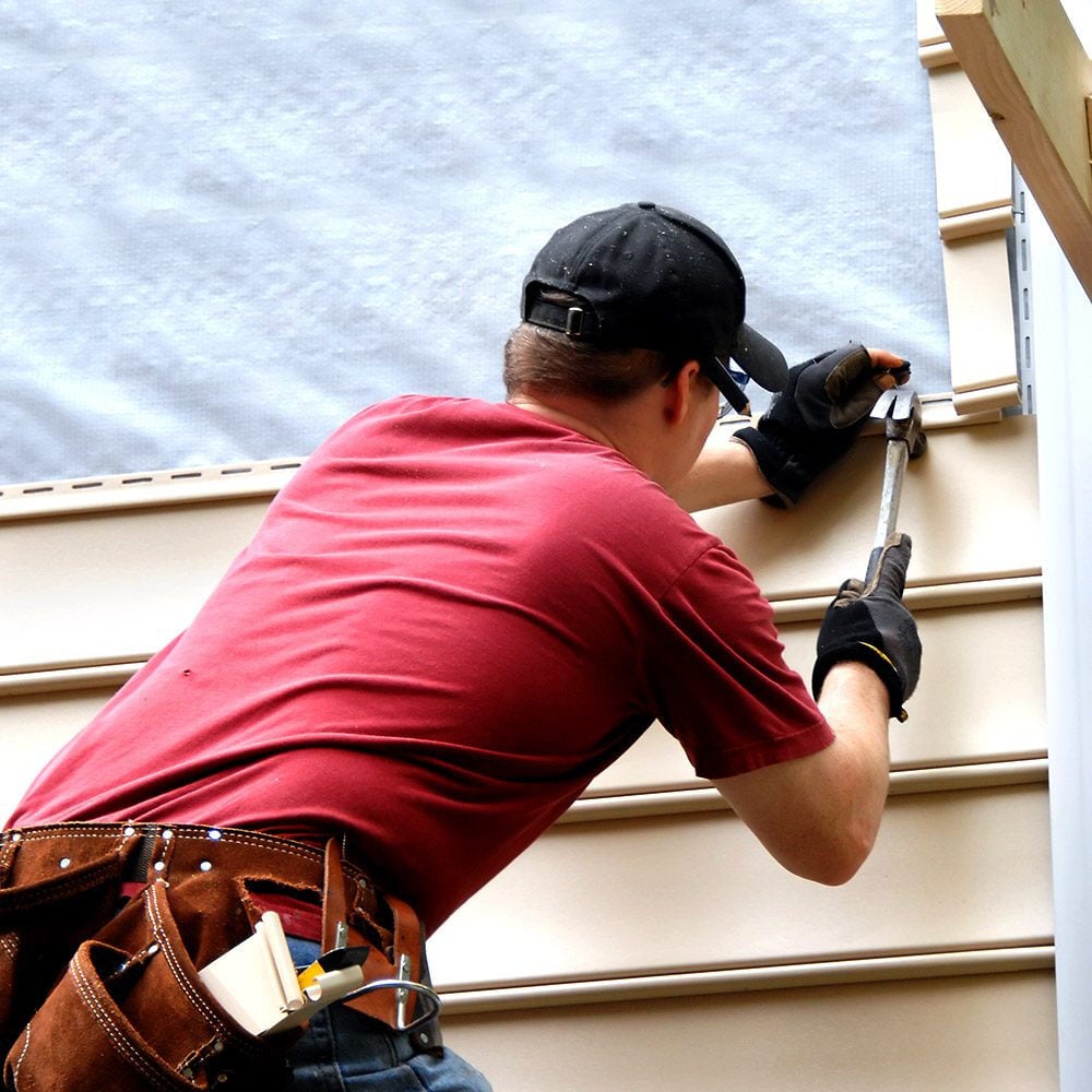 A man in a red shirt and black cap installing siding