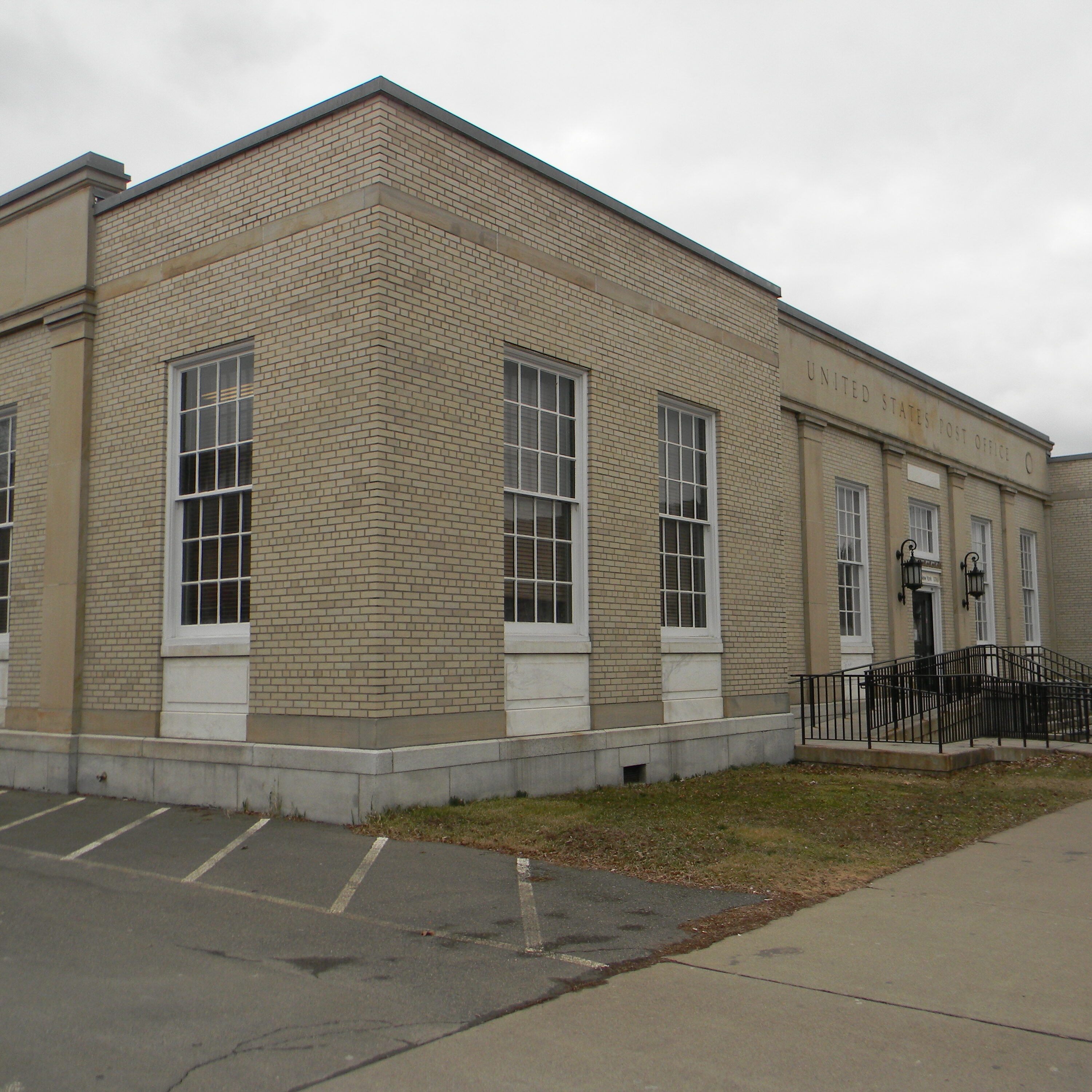 A tan brick institutional building featuring multiple windows, a covered entrance, and an American flag.