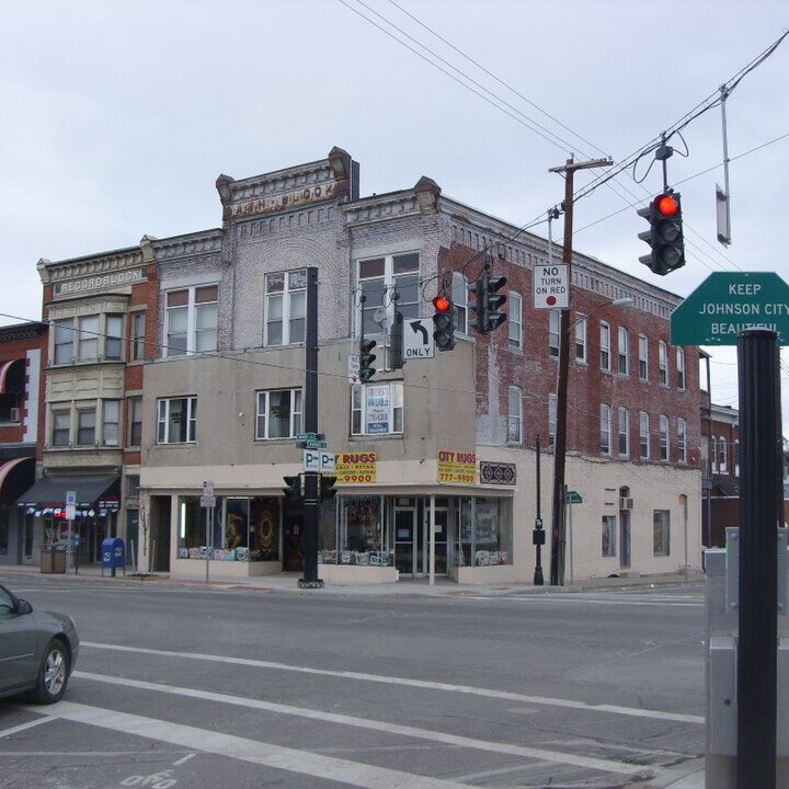 A city intersection showing a multi-story brick building, a traffic light, and a small green signpost.
