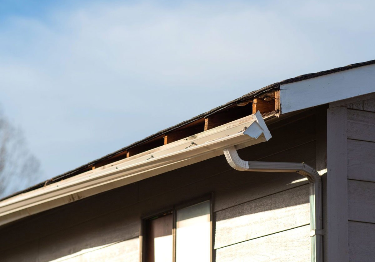 A house roof edge with a gutter system. The roof edge has some wood damage.