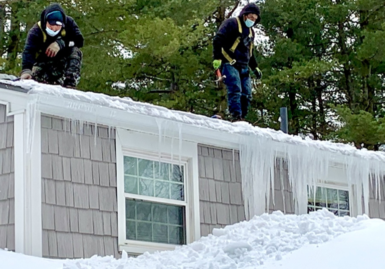 Two workers on a roof clearing ice and snow. They are focused on their task.