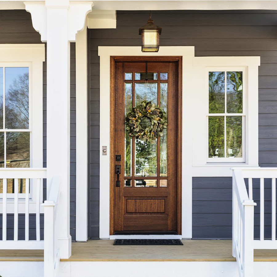 Brown wooden front door with glass panels and a wreath. The door is flanked by two windows.