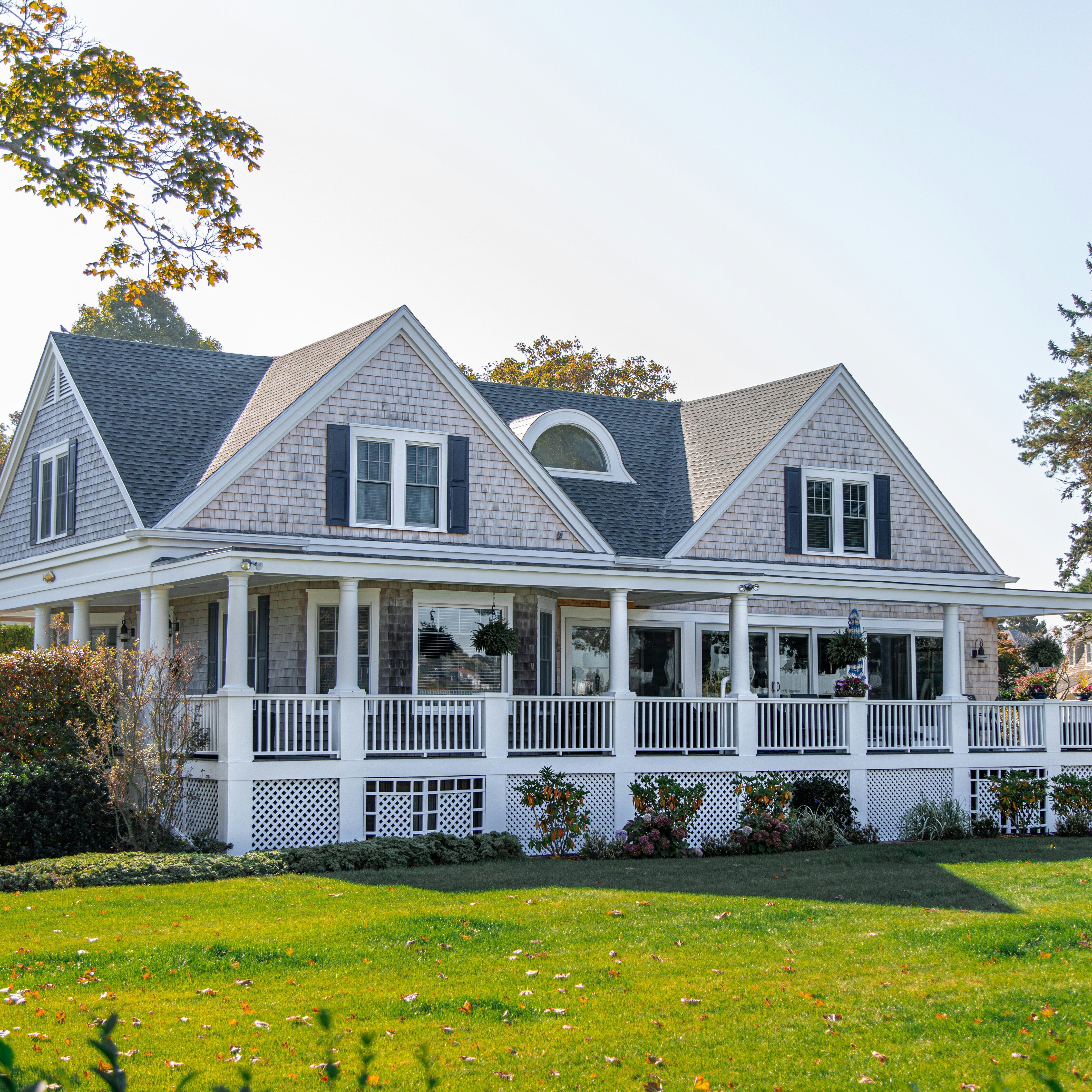 A large white house with a big front porch and green lawn. The house has a classic design with a gray roof.