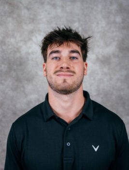 A young man with dark hair and a short beard wearing a black polo shirt with a white logo